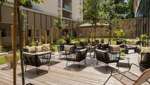 An outdoor patio area with wicker furniture, a wooden deck, and a brick wall in the background. - Residhome Toulouse Ponts Jumeaux (Toulouse)