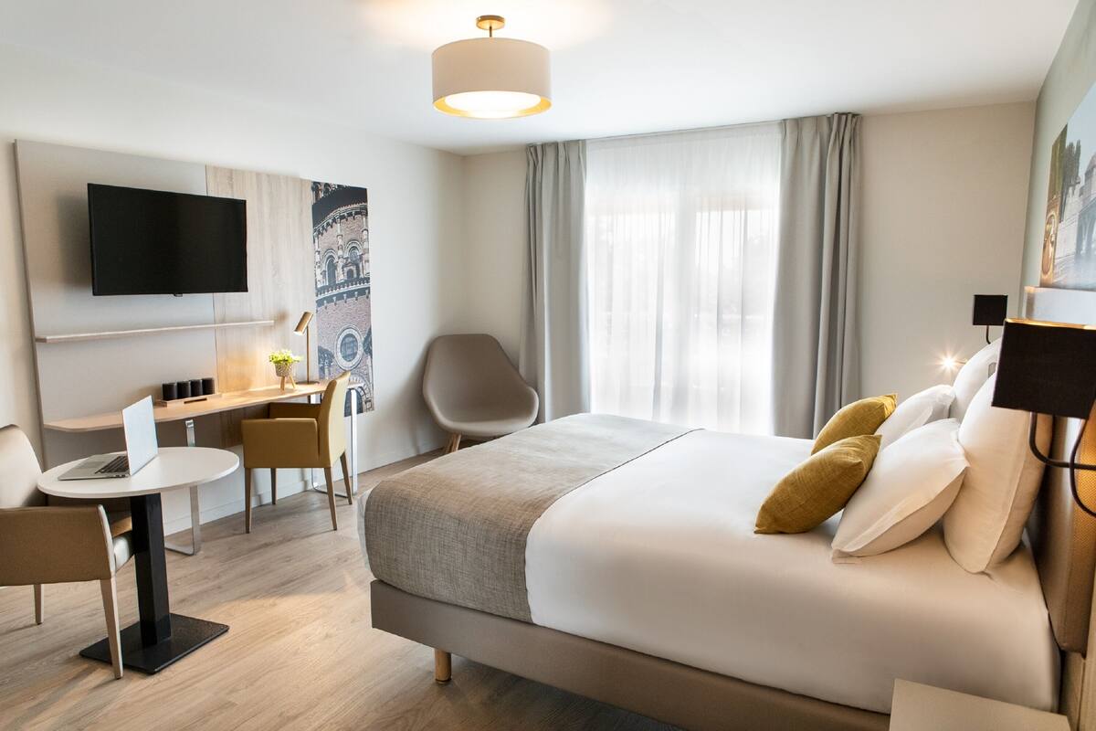 Ein Hotelzimmer mit Bett, Schreibtisch, Stuhl, Fernseher und Lampe.