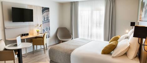 A hotel room with a bed, a desk, a chair, a television, and a lamp.