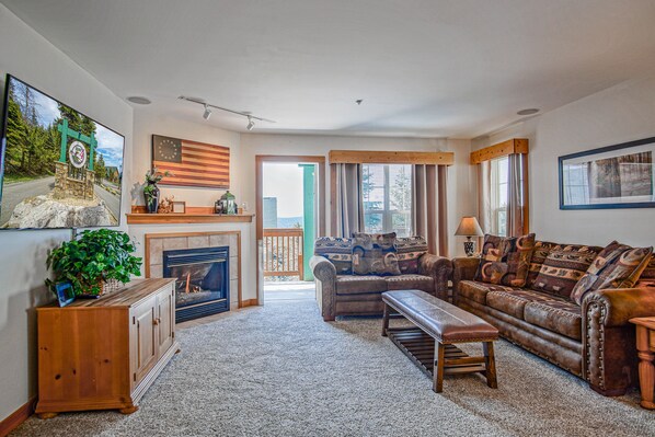 A living room with a fireplace, a sofa, a bench, and a wooden cabinet. - Camp 4 #1 3 bedroom, 3.5 bath (Snowshoe)