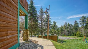 Eine Holzhütte mit Steinfundament, einem Betonweg und einem bewaldeten Gebiet mit hohen Bäumen.