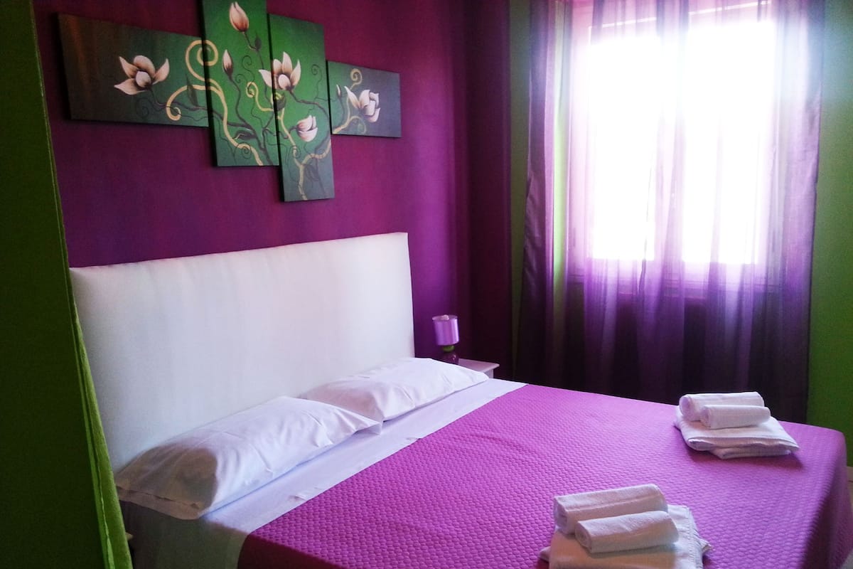 A bed with white linens, a purple bedspread, and towels on the side.