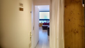 Un pasillo con techo de madera, una puerta con placa de identificación y vista a una habitación con cama y ventana.