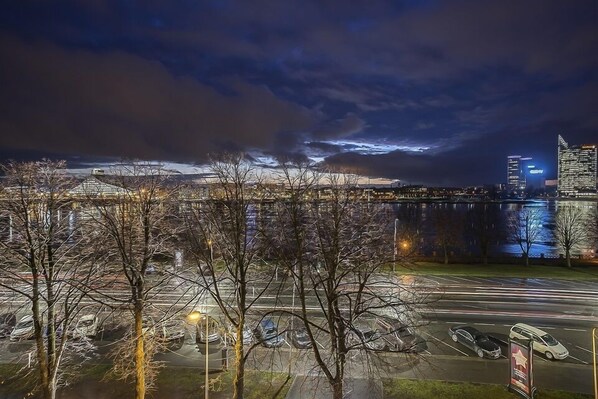 A nighttime cityscape with a river, a bridge, and a parking lot.
