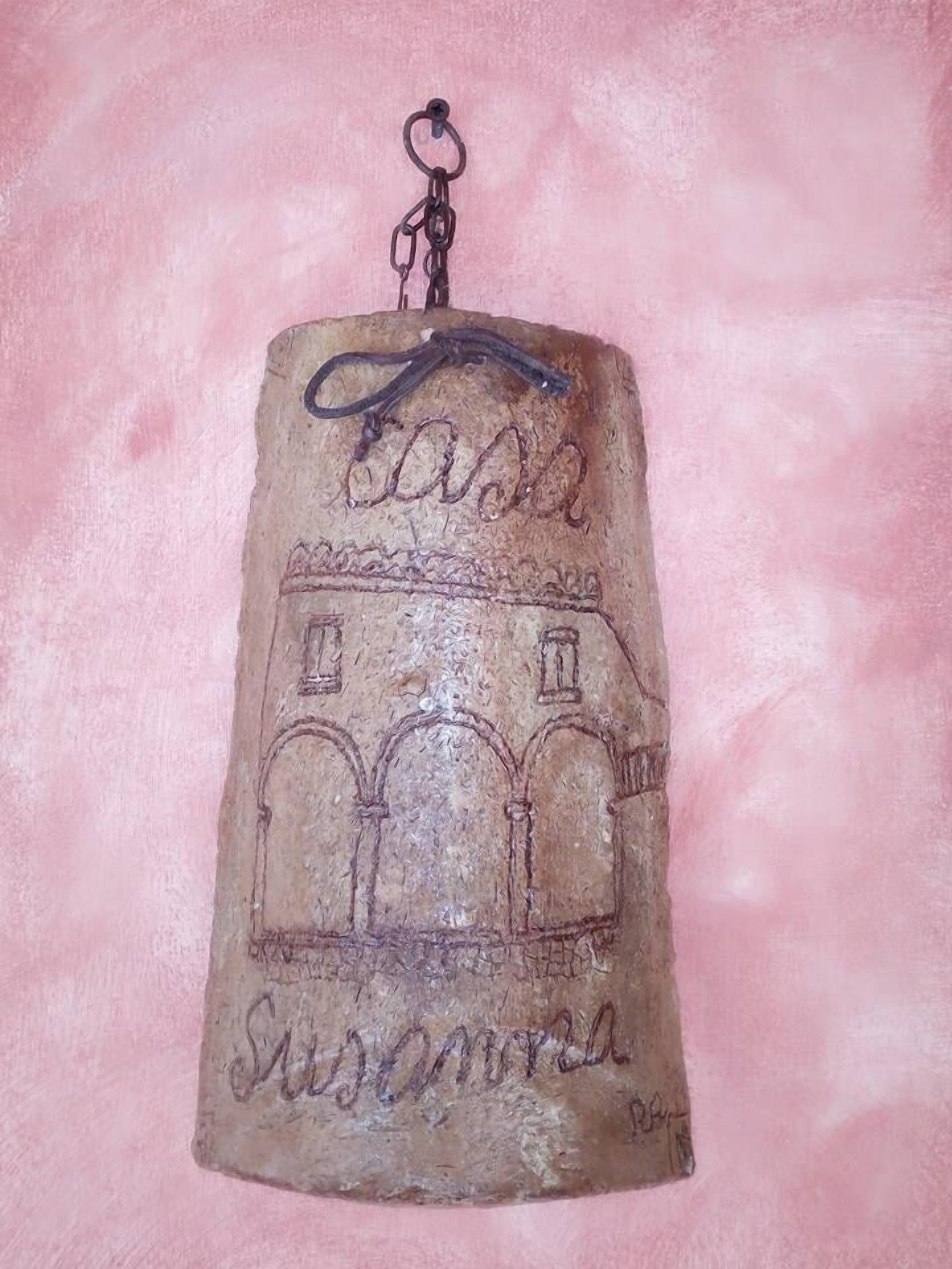 A cylindrical object with a metal ring at the top, featuring a building sketch and the word "SUSANA" at the bottom.