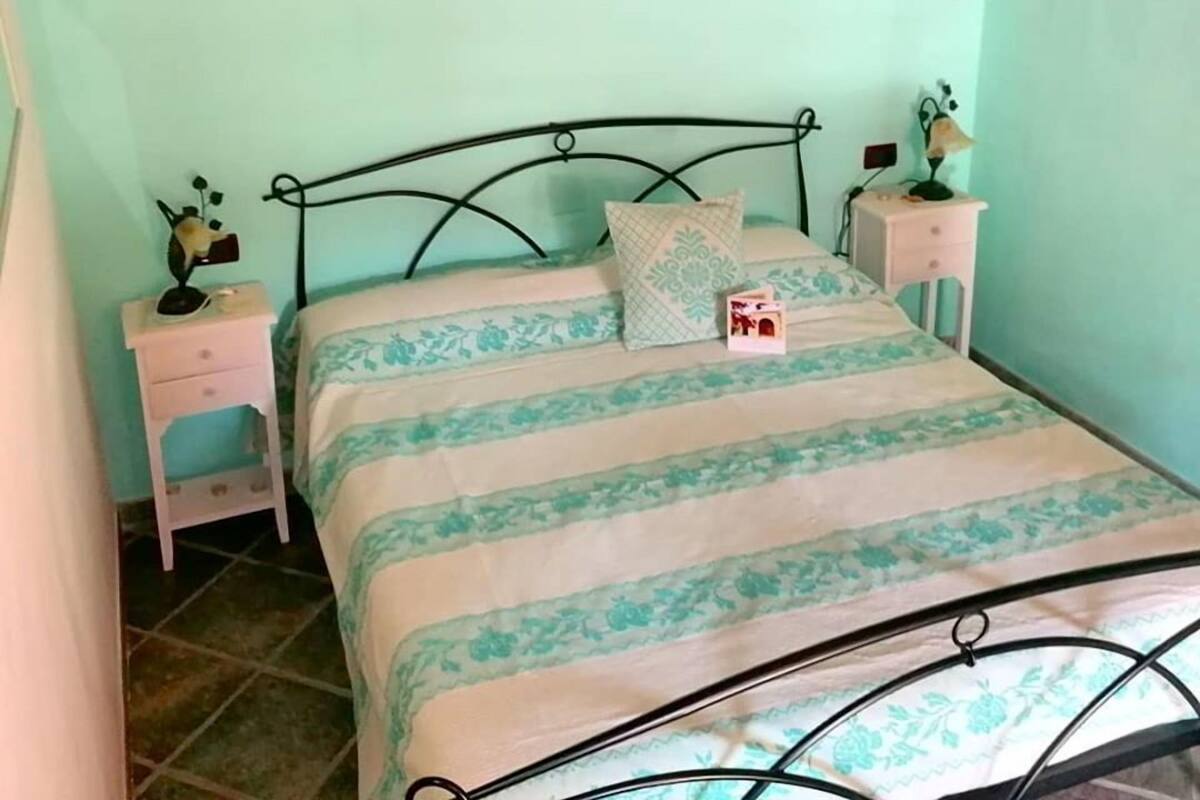 A bedroom with a bed, two bedside tables, a nightstand, a wall-mounted shelf, and a decorative brick wall piece.