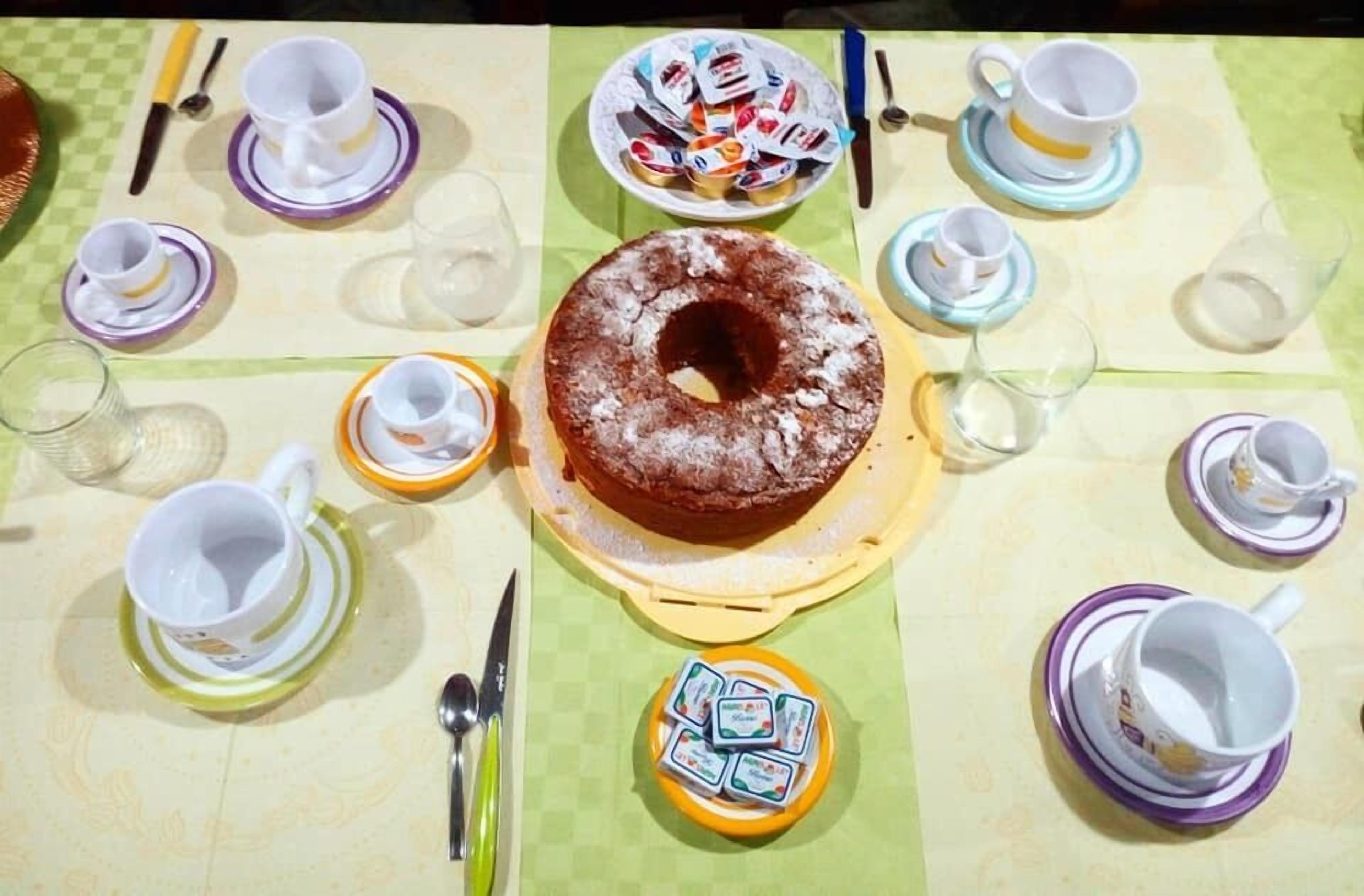 Una mesa dispuesta para una comida, con un pastel central, varias tazas y platitos, y un pequeño recipiente con salsas.