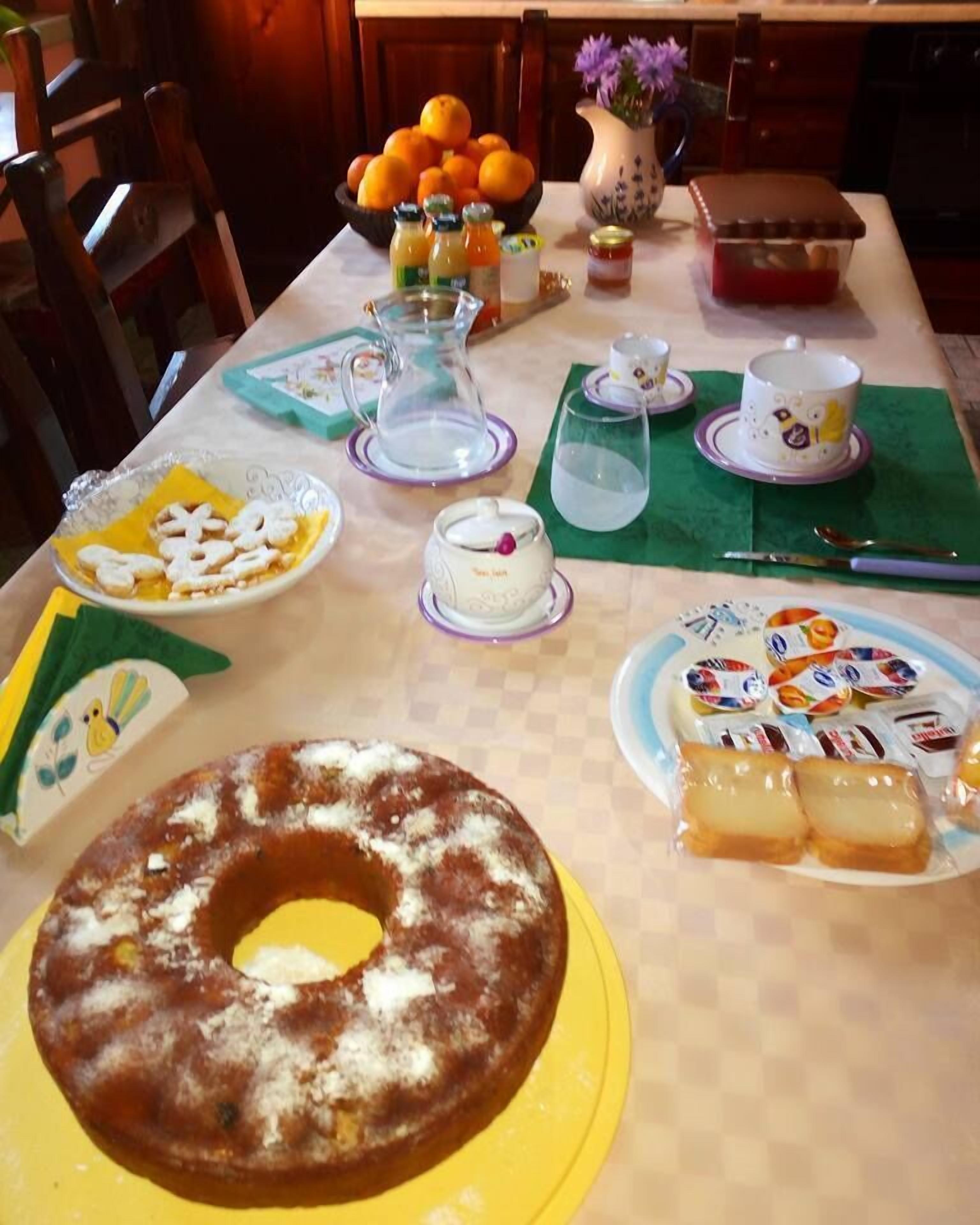 A dining table with various food items, including a bundt cake, pastries, and a bowl of oranges.