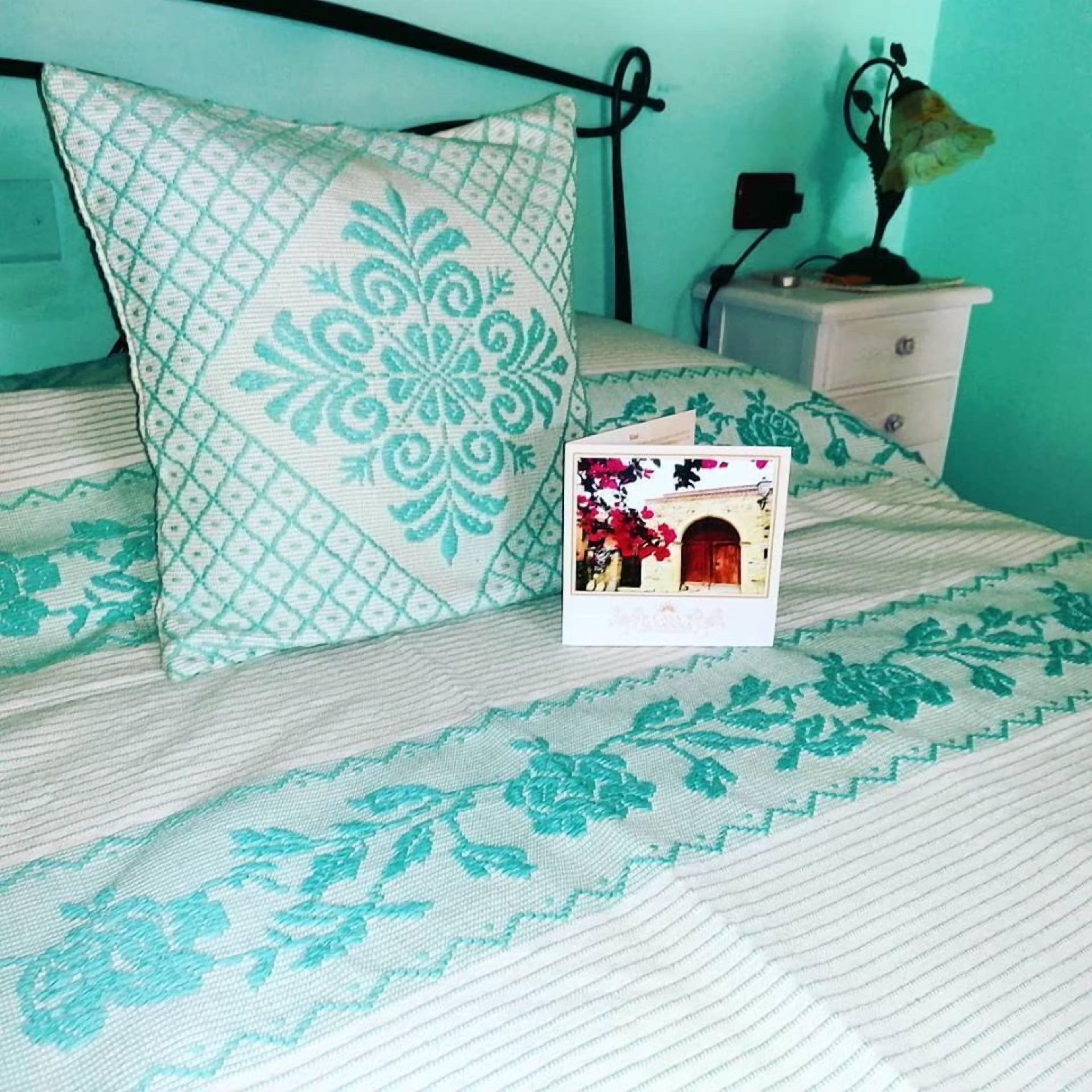 Una cama con ropa de cama estampada, una almohada, una mesita de noche con lámpara y un pequeño marco de fotos.