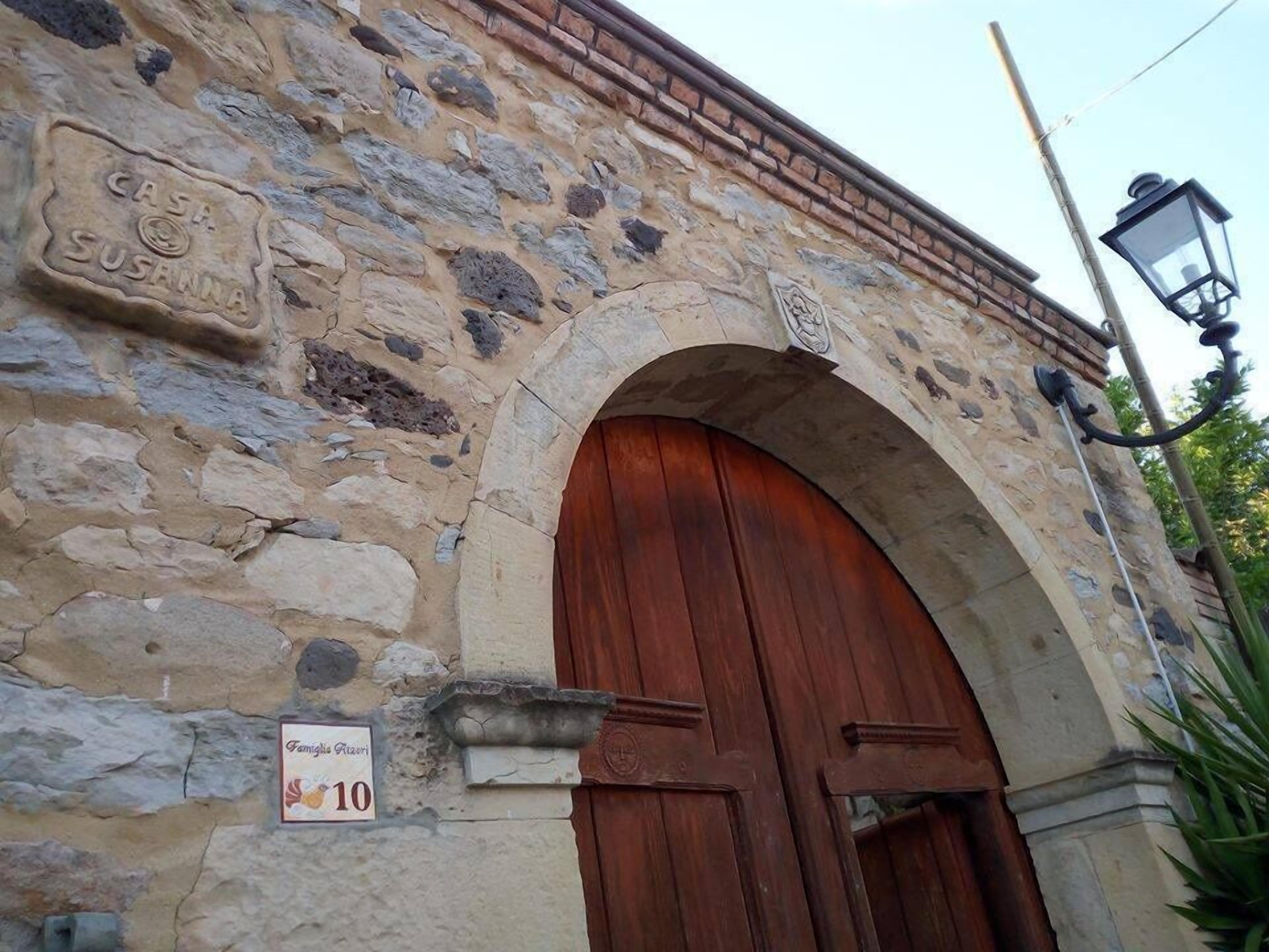 Ein Steinhaus mit einer großen Holztür, einem Schild mit der Aufschrift 'Famiglia Ruzini' und einem Laternenpfahl.
