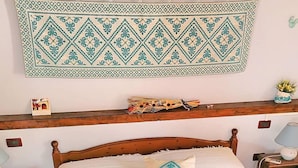 A neatly made bed with a decorative pillow, a wall hanging above, and a wooden headboard.