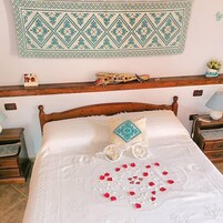 Una cama bien tendida con un cojín decorativo, un adorno en la pared y una cabecera de madera.
