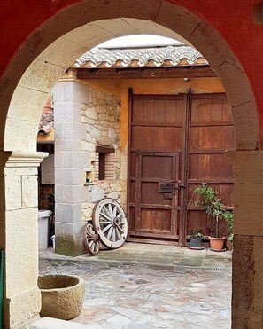 Una entrada arqueada con un muro de piedra, una puerta de madera y una planta en maceta.