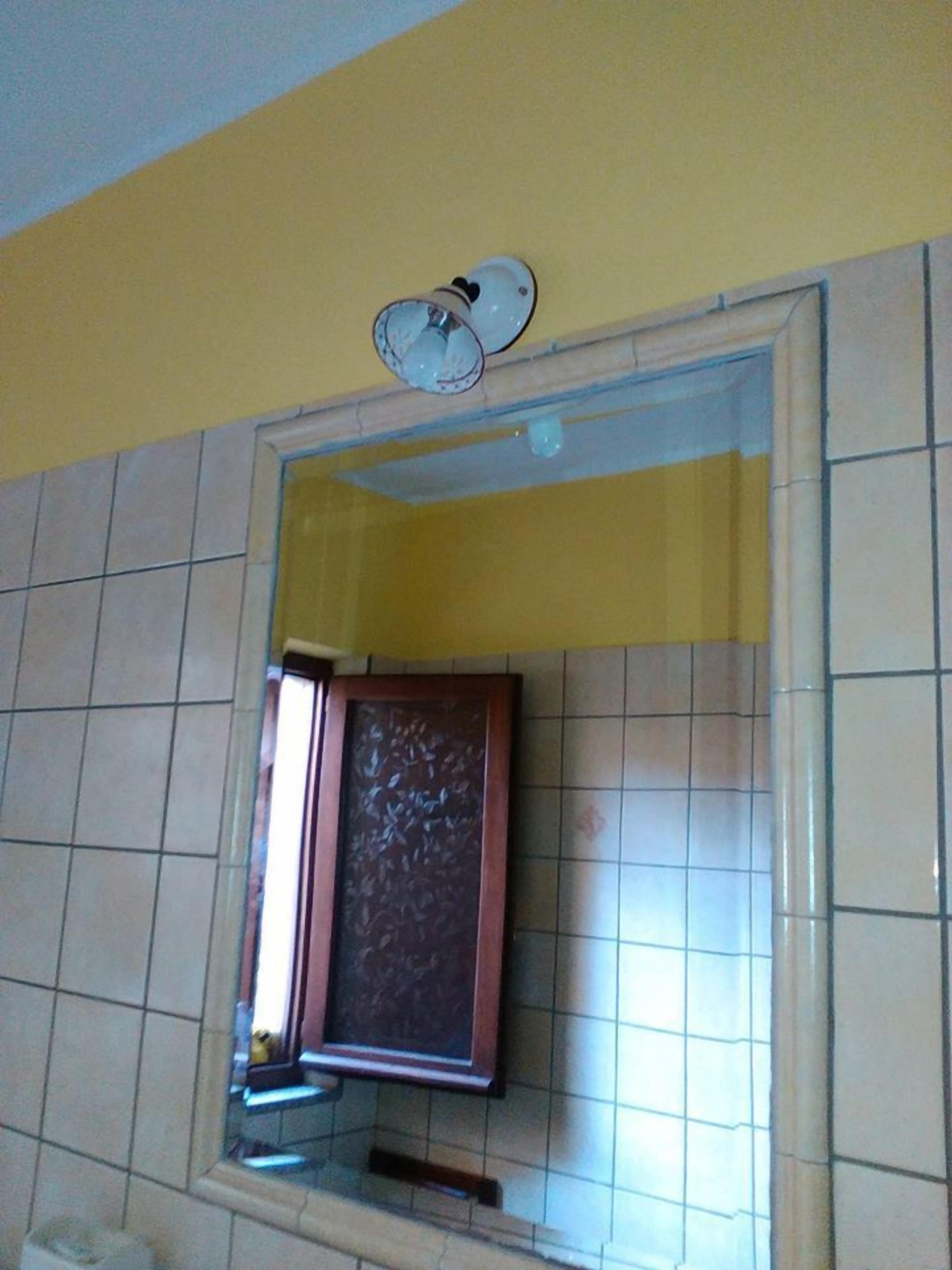 Ein Badezimmer mit gefliesten Wänden, einem Spiegel und einer Deckenleuchte.
