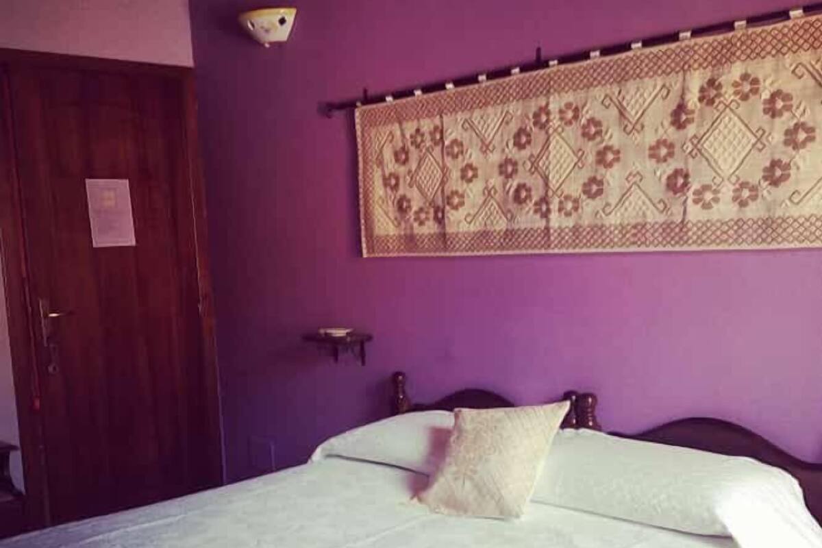 A room with a bed, a wooden door, and a wall hanging.