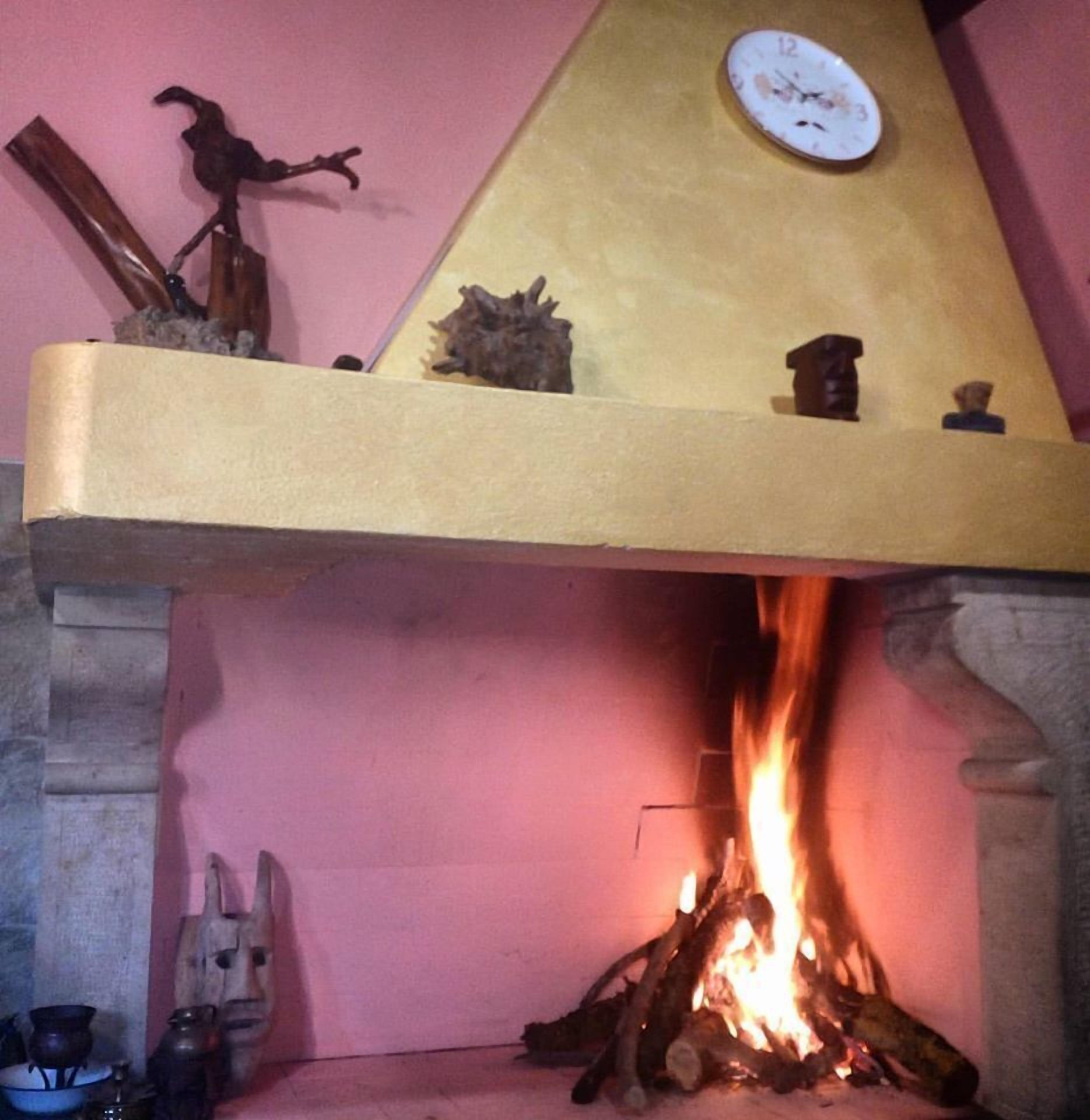 A fireplace with a clock above it, a wooden sculpture, and a mask on the wall.