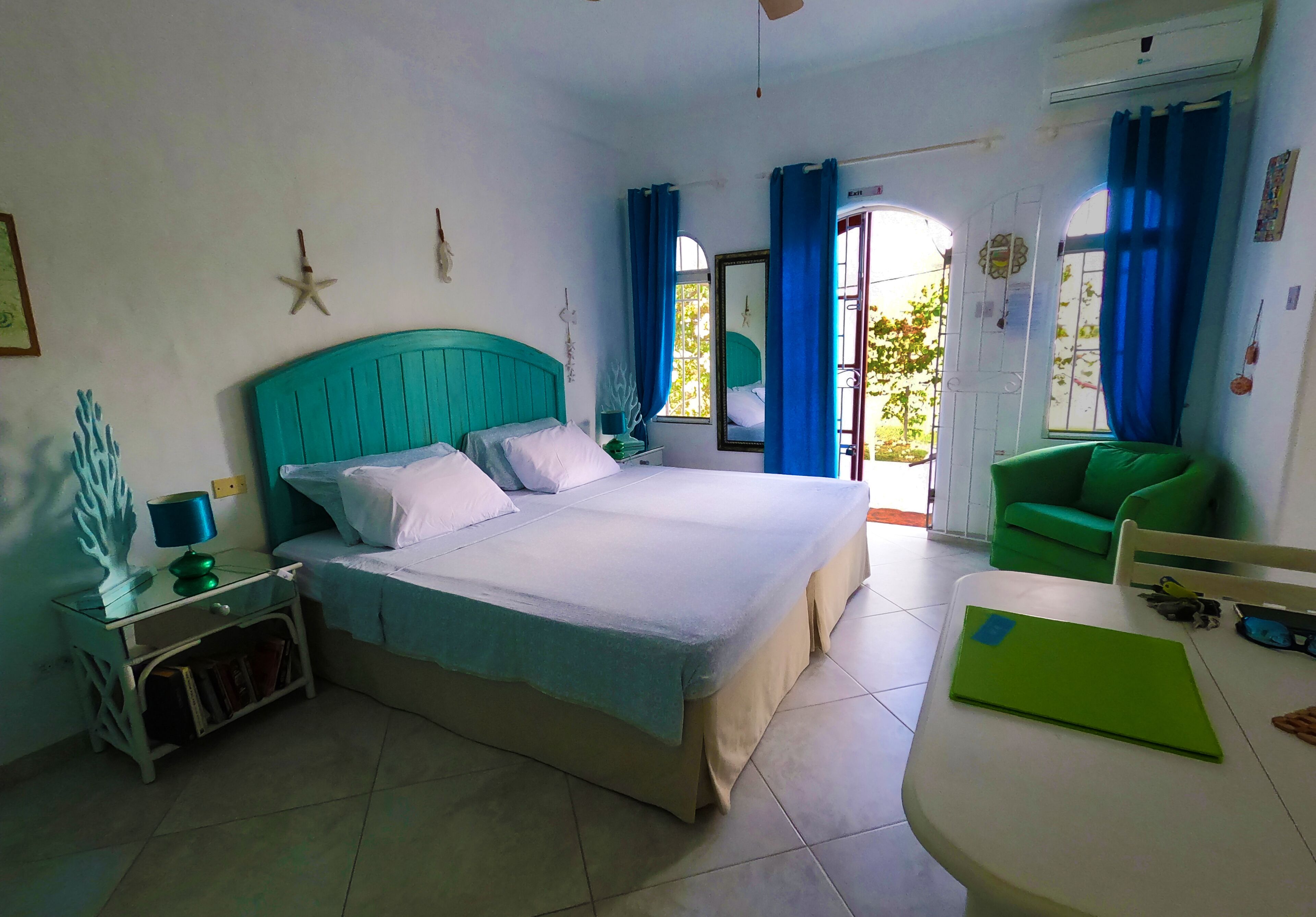 Un dormitorio con cama, mesita de noche, silla verde y una mesa.