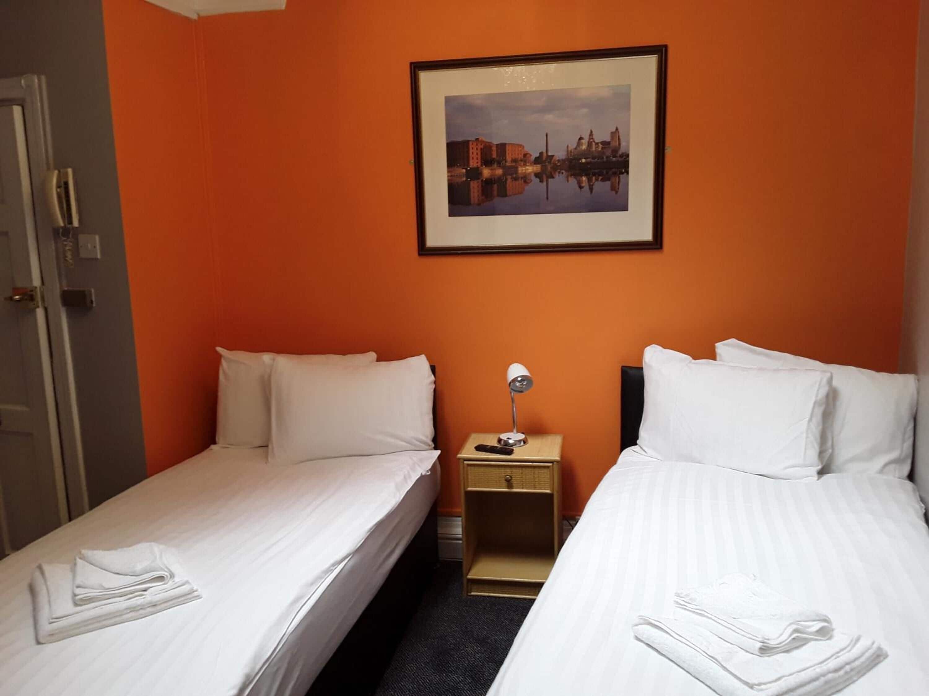 Een hotelkamer met twee eenpersoonsbedden, een nachtkastje met een lamp en een lijst met een stadsbeeld aan de muur.
