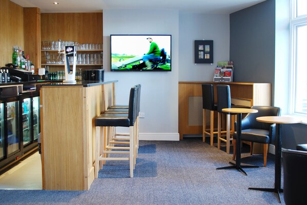A bar area with a television mounted on the wall, bar stools, and a seating area with tables and chairs. - The Liverpool Inn Hotel (Liverpool)