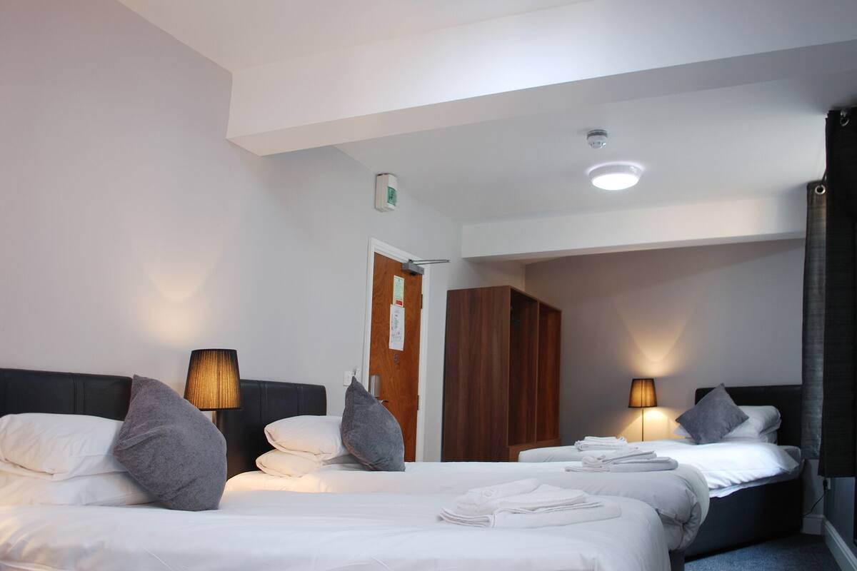 A hotel room with two beds, a wooden wardrobe, a door with a notice, and a ceiling light.