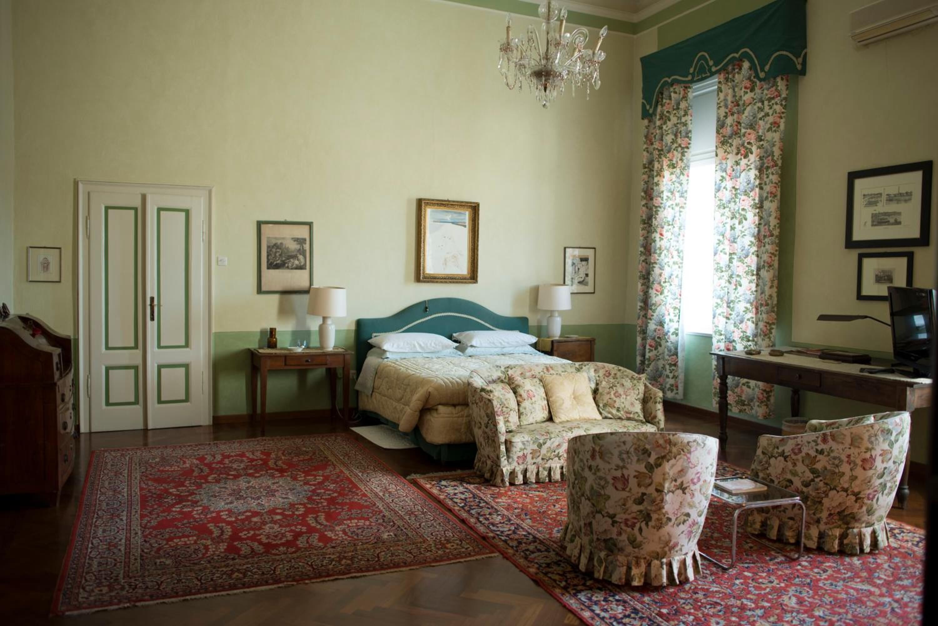 A bedroom with a bed, two nightstands, a desk, a chair, and a chandelier.