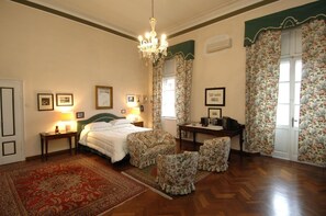 Un dormitorio con cama, dos mesitas de noche, un escritorio, una silla, una araña y cortinas con estampado floral.