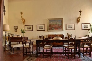 Un comedor con una mesa y sillas de madera, cuadros en la pared y un cuadro grande sobre la mesa.