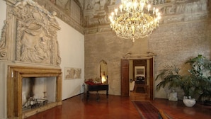 A grand hall with a large chandelier, ornate wall carvings, a fireplace, and a mirror.