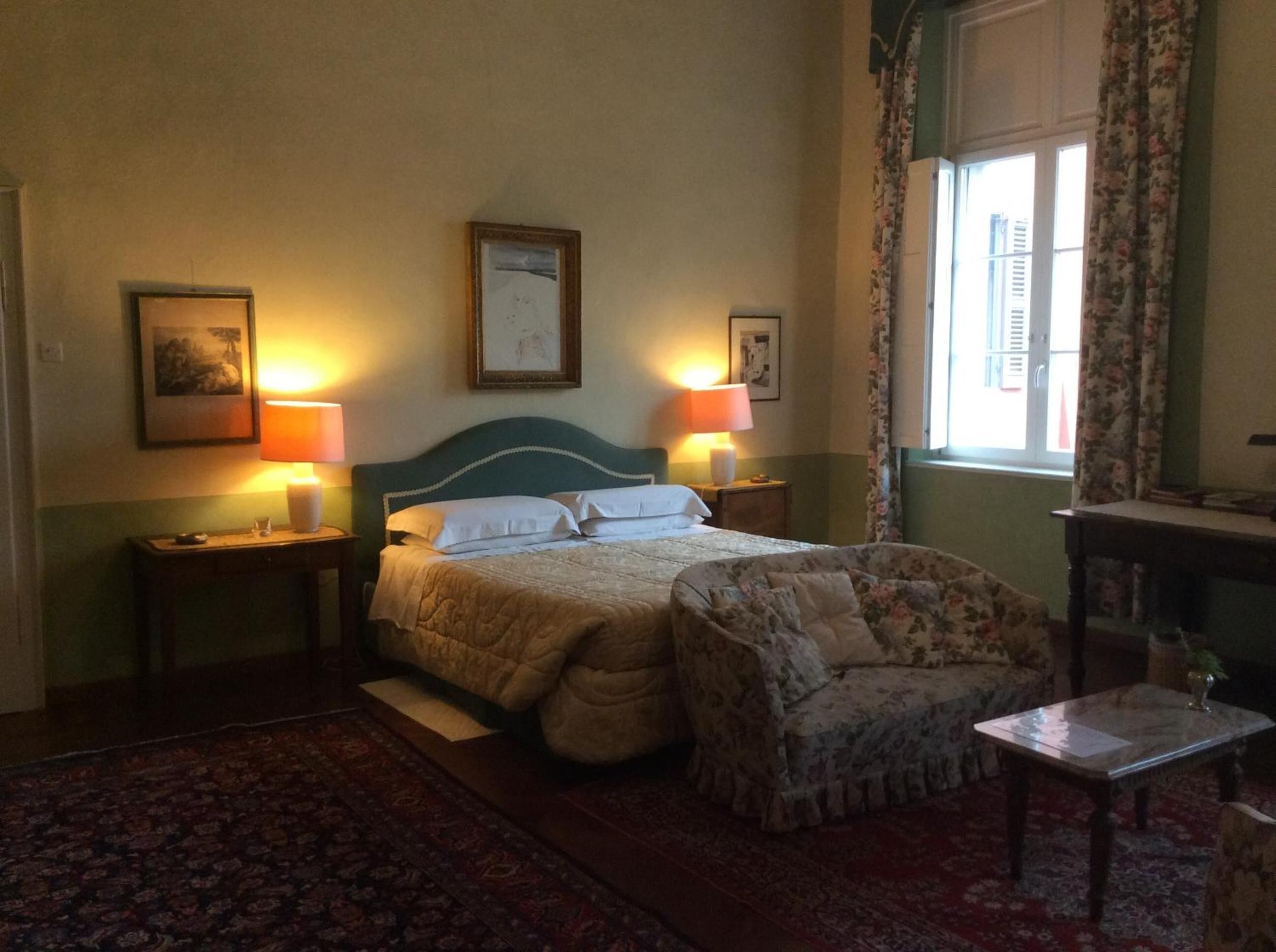 A bedroom with a bed, two bedside lamps, a chair, a small table, and a window with curtains.
