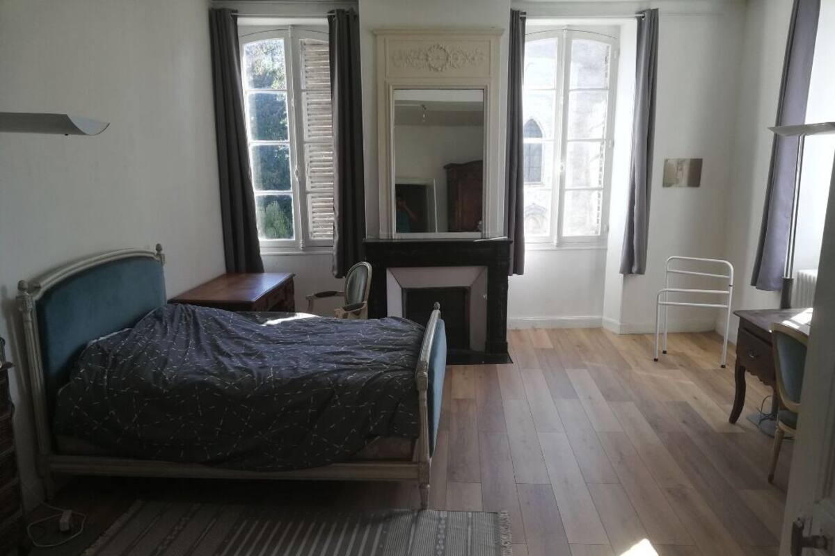 Ein Schlafzimmer mit Bett, Schreibtisch, Stuhl, Heizkörper und einem Fenster mit Vorhängen.