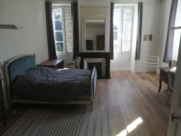 A bedroom with a bed, a desk, a chair, a radiator, and a window with curtains.