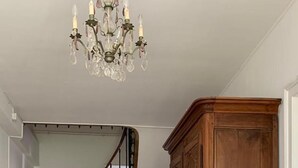 A spacious hallway with a wooden staircase, a large wooden cabinet, and a chandelier. - Grand Corps de Ferme (Branches)
