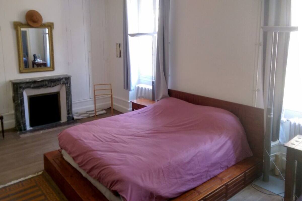 Ein Schlafzimmer mit einem großen Bett, einem Sessel, einem Kamin und einem Fenster mit Vorhängen.