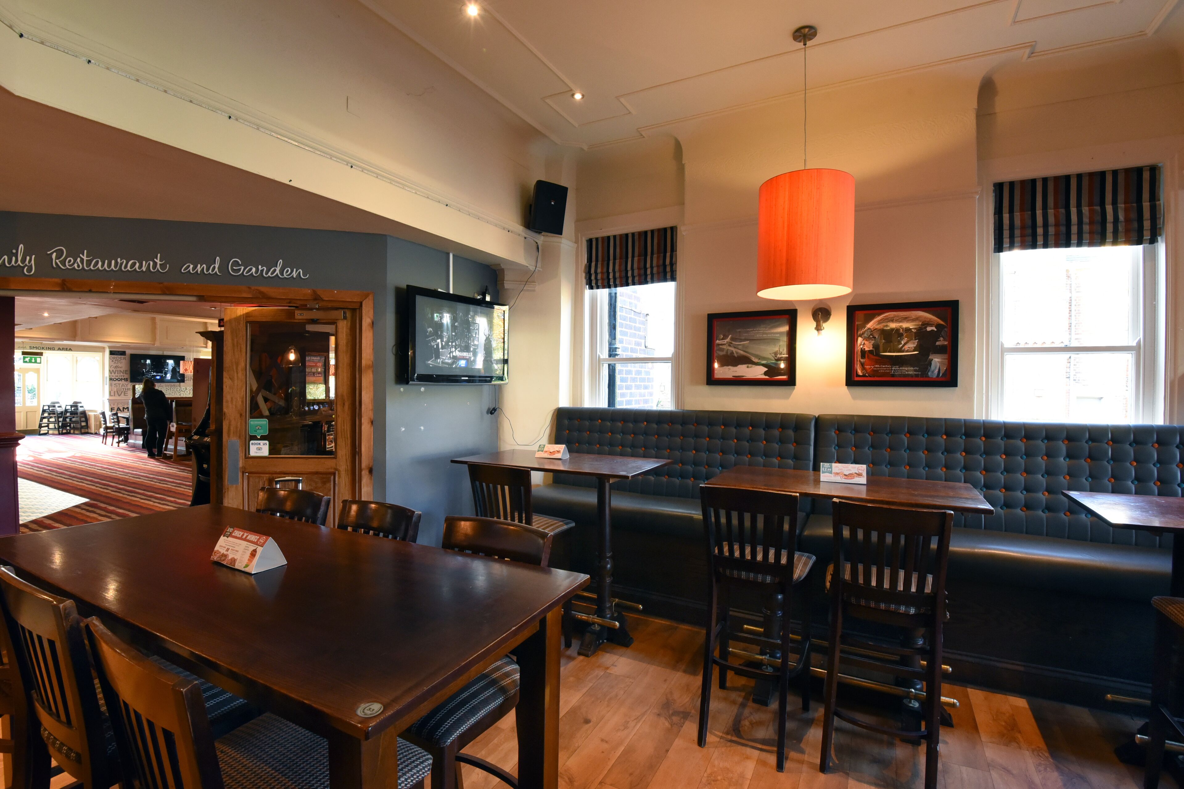 A restaurant interior with wooden tables and chairs, a black cushioned bench, and a red pendant light.