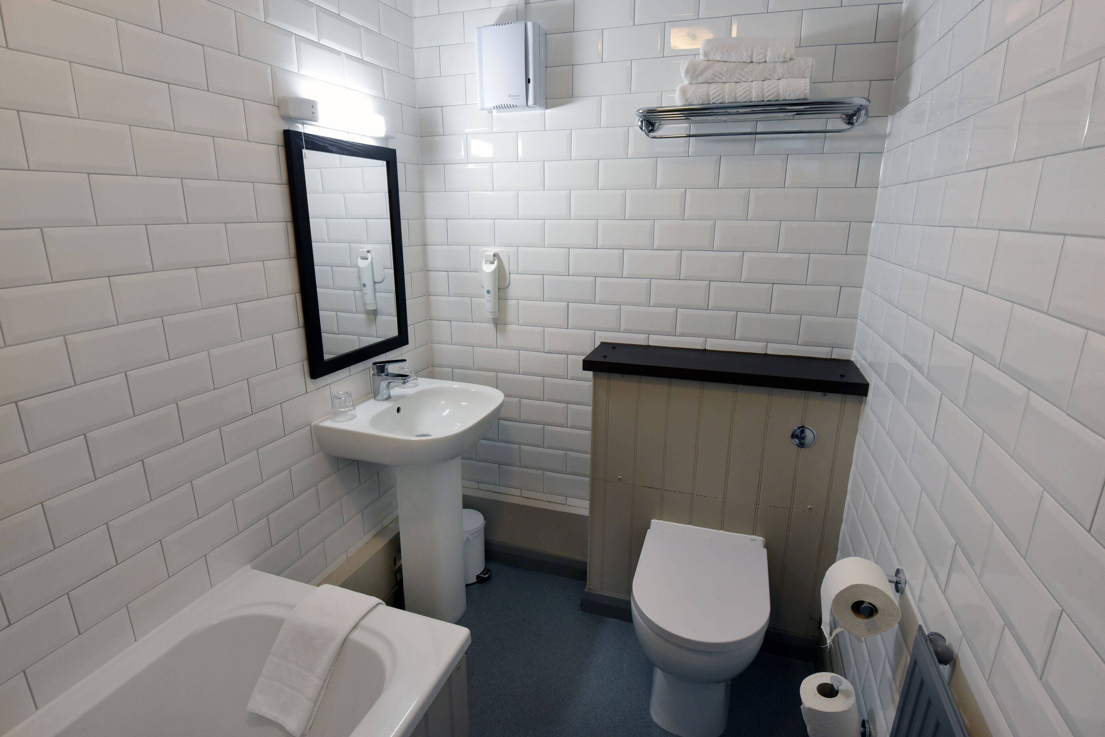 Ein Badezimmer mit weißen Fliesen, einem Waschbecken, einer Toilette und einer Badewanne.