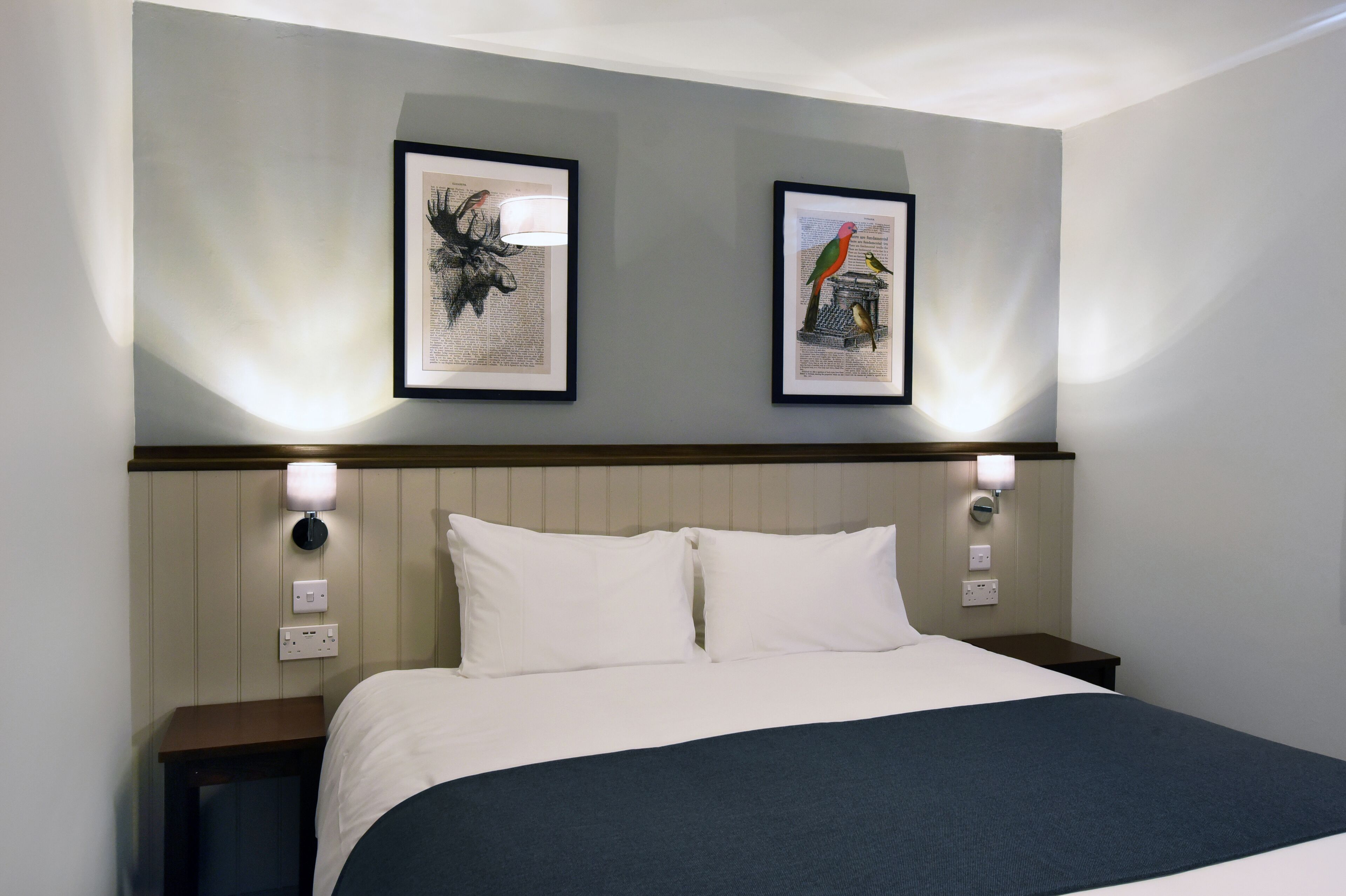 A hotel room with a bed, two framed pictures on the wall, and bedside lamps.