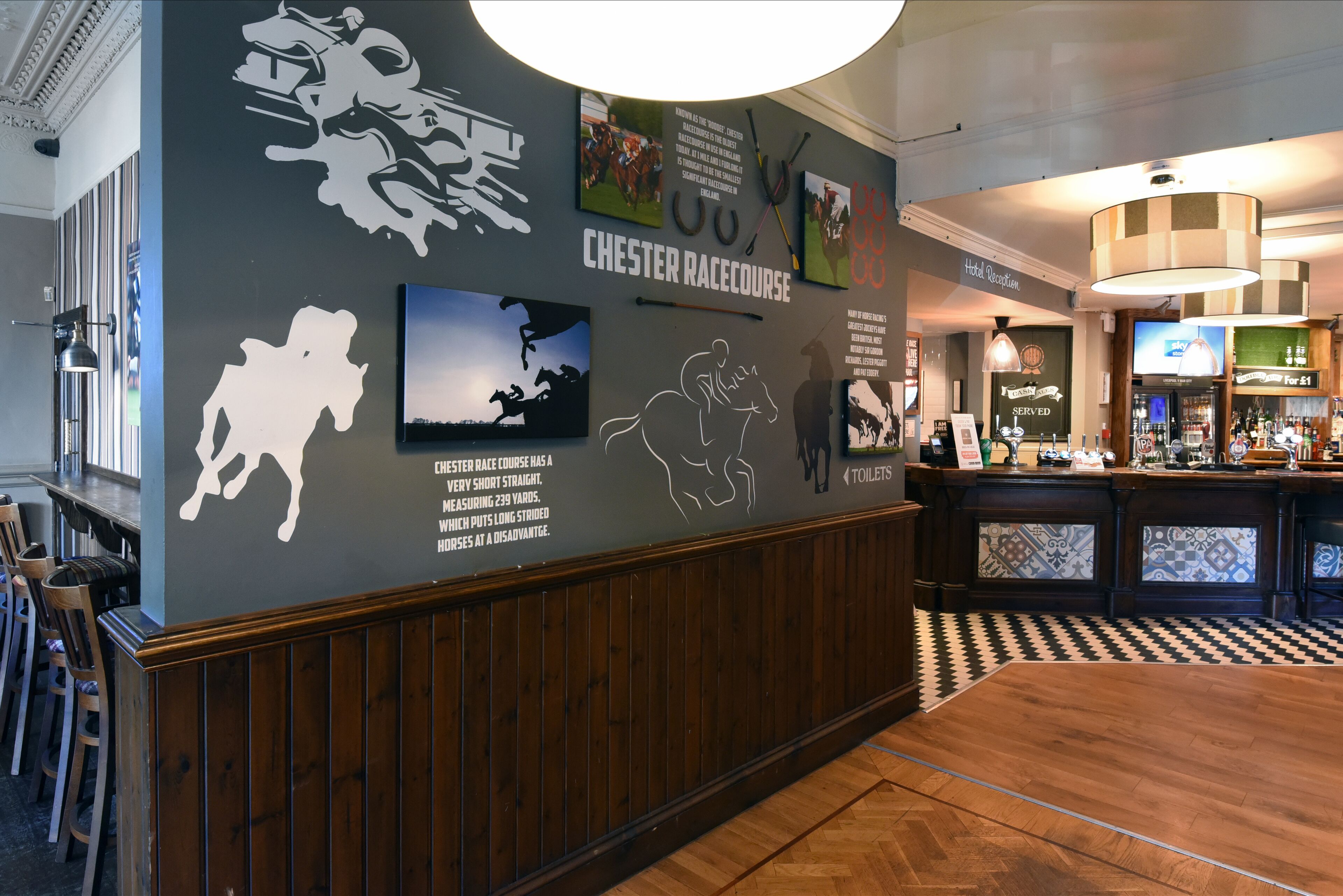 A hotel lobby with a racecourse theme, including wall art and a bar area.