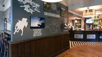 A hotel lobby with a racecourse theme, including wall art and a bar area.