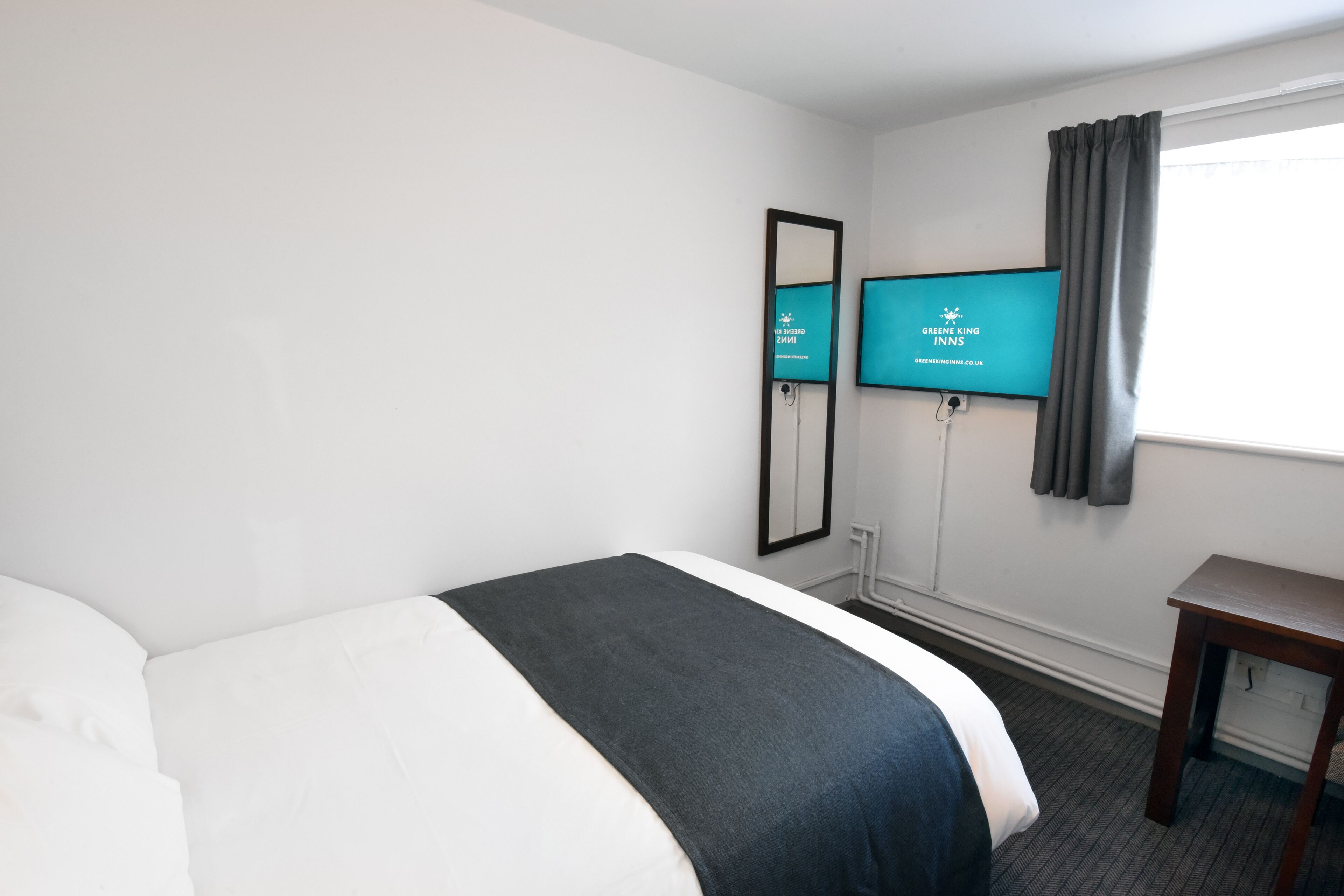 Una habitación de hotel con una cama, televisión, escritorio y ventana con cortinas.