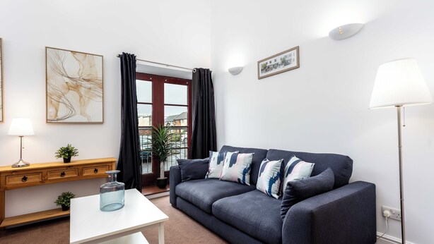 Ein modernes Wohnzimmer mit einem dunkelblauen Sofa, einem weißen Couchtisch, einem Holznachttisch mit Lampe und einer Stehlampe.