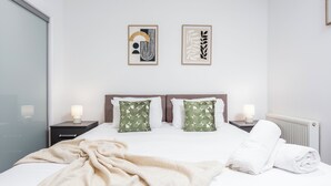 Ein ordentlich bezogenes Bett mit einer beigen Decke, zwei Kissen mit einem grünen Blattmuster und zwei Nachttischlampen.