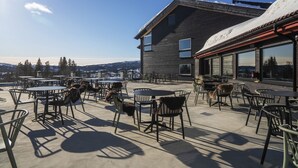 An outdoor patio with tables and chairs, a building with large windows, and a snowy mountain view. - Skeikampen Servicesenter (Gausdal)
