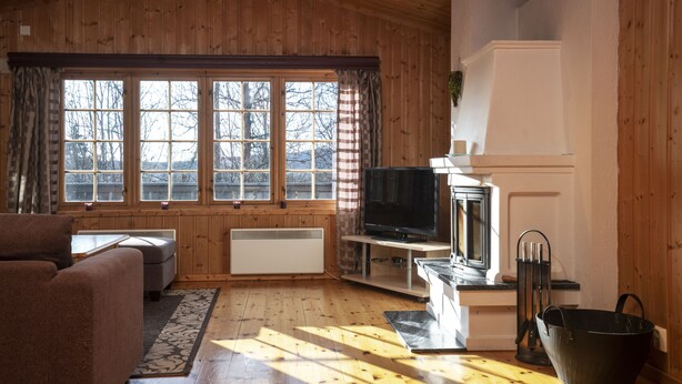 A cozy cabin interior with a wooden interior, a fireplace, a television, and a large window with curtains. - Skeikampen Servicesenter (Gausdal)