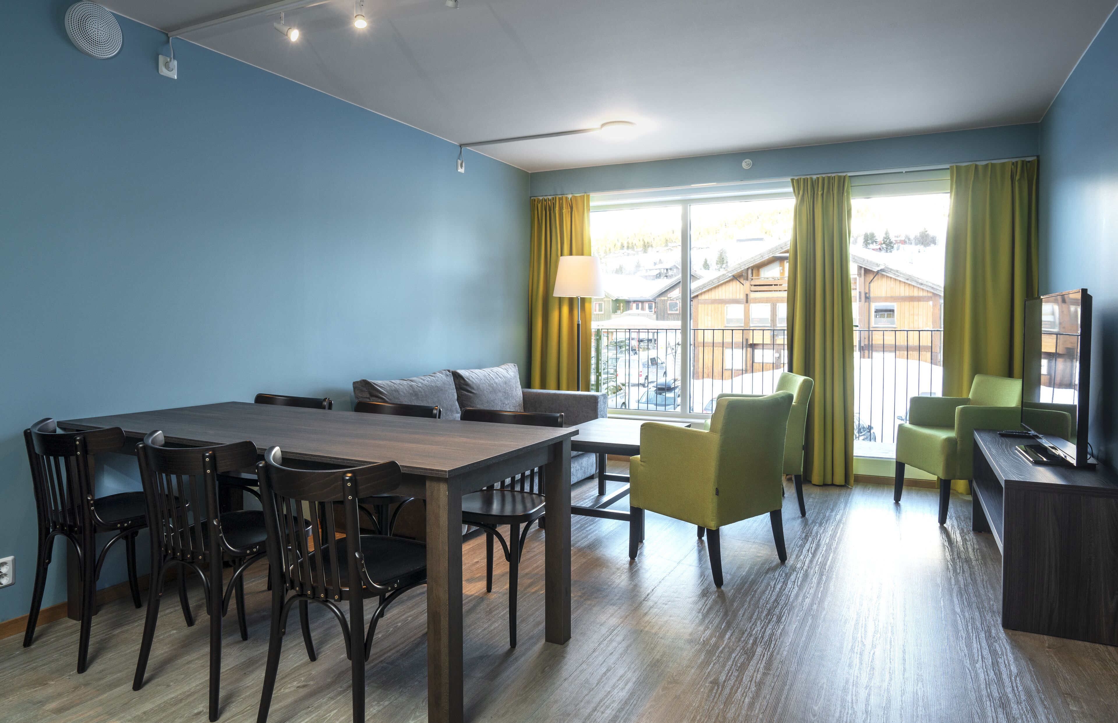 Un salon moderne avec un coin repas, de grandes fenêtres avec des rideaux et une vue sur les bâtiments environnants.