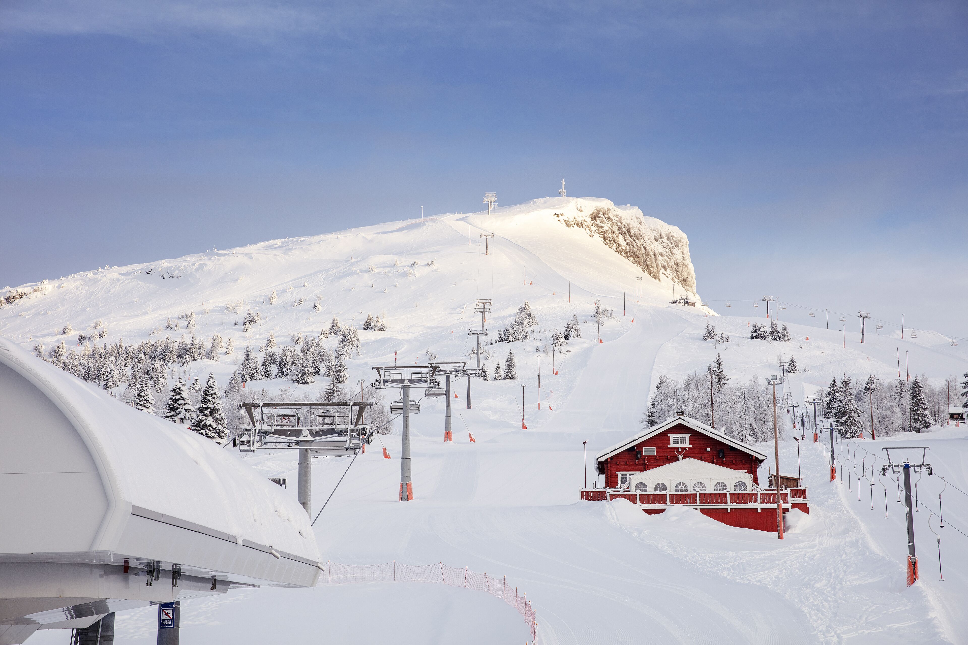A snow-covered ski slope with a red chalet and a ski lift.