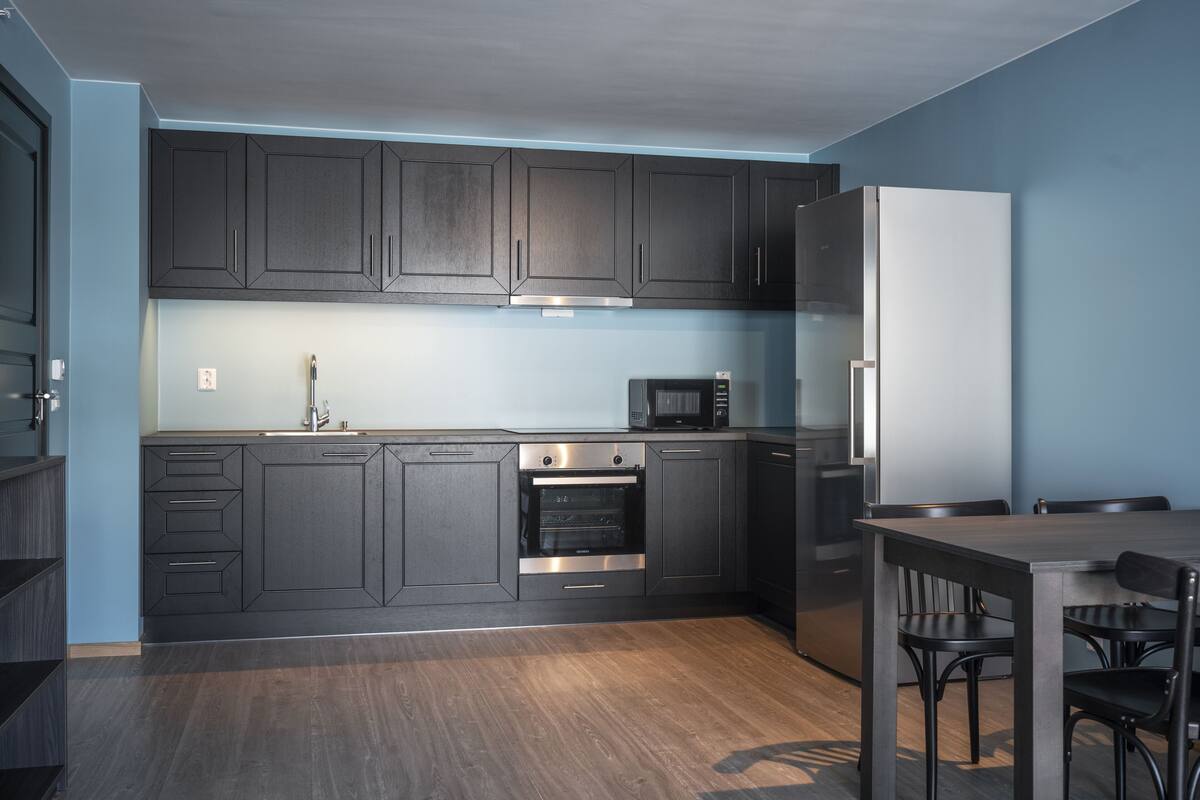Una cocina moderna con armarios oscuros, electrodomésticos de acero inoxidable y piso de madera.