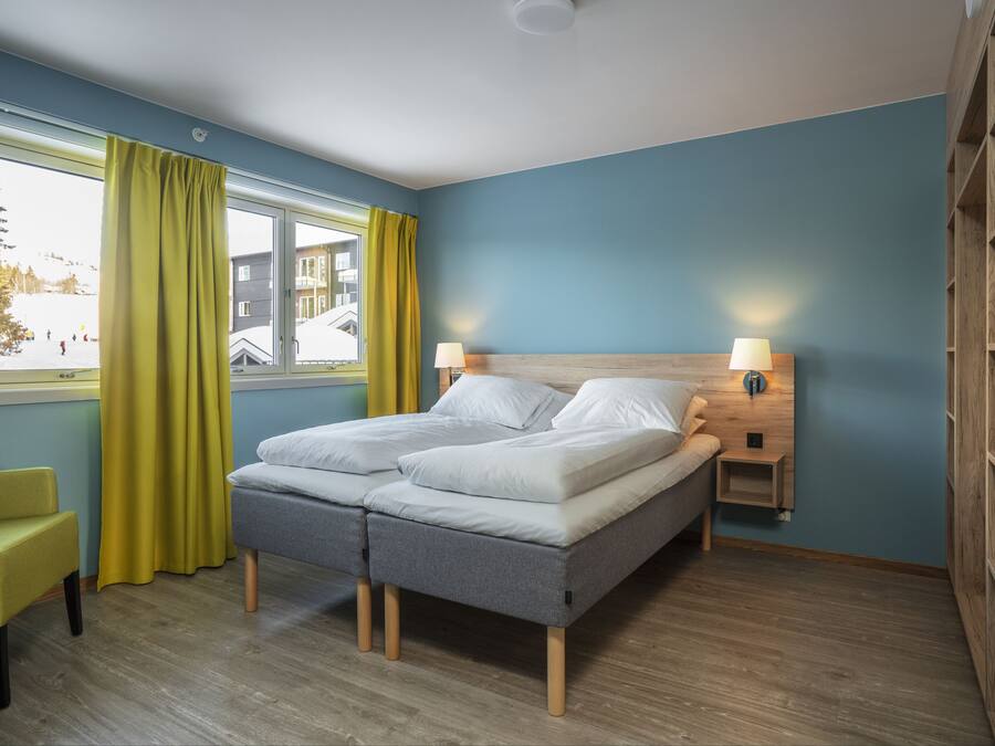 Un dormitorio con una cama, dos mesitas de noche, una silla y una ventana con cortinas.