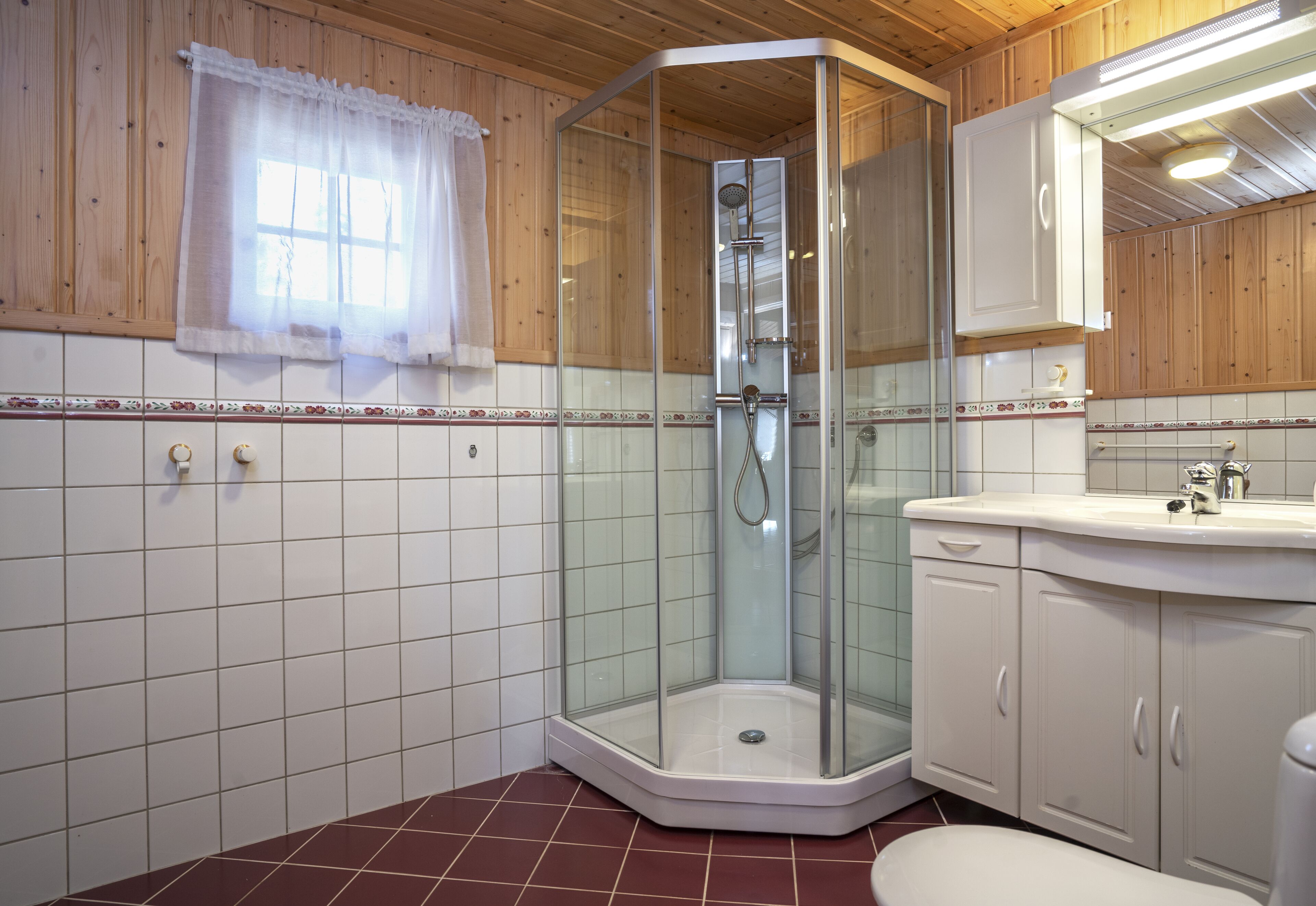 Eine Eckdusche mit Glastüren, ein weißes Waschbecken und eine Wand mit Holzpaneelen.