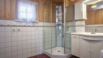 Eine Eckdusche mit Glastüren, ein weißes Waschbecken und eine Wand mit Holzpaneelen.