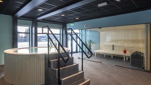 A modern lobby with a curved reception desk, a staircase with metal railings, a seating area with a bench, and a glass partition. - Skeikampen Servicesenter (Gausdal)